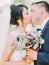 Beautiful wedding bouquet of colourful peonies with herbs in the hands of kissing newlyweds.