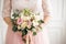 Beautiful wedding bouquet in hands of the bride. Rose, pink and Peach. Trendy and modern wedding flowers. Woman in wedding dress