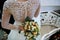 Beautiful wedding bouquet with white flowers and green leaves in the hands of the bride and groom in a dress with a lace back