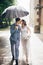 Beautiful wedding couple embracing together under umbrella in sunny rainy street. Stylish bride and groom walking and kissing on