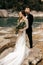 Beautiful wedding couple tenderly hug on the background of a mountain river, long white dress of the bride