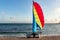 Beautiful white catamaran with red and yellow and blue sail and equipment is on the gold beach on the wet sand by turquoise sea on