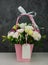 Beautiful white Eustoma Gypsophila flowers bouquet in pink pastel basket dark background. Floral gift blooming wallpaper