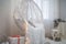 Beautiful white lace cocoon chair with plaid and cushion, golden garland lights in room decorated for Christmas. Magic Christmas