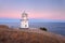 Beautiful white lighthouse on the ocean coastline at sunset. Landscape