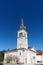 Beautiful white neoclassical style church with cock and bell tower against clear blue sky