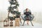 Beautiful white room. Christmas and holidays conception. Cute little girl is sits on the chair near ladder decorated