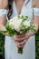Beautiful white rose bouquet with baby`s breath held by a bride with dark hair wearing a white wedding dress and an engagement rin