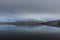 Beautiful wide shot of the reflection of snowy mountains in the water under a gray sky