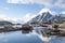 Beautiful winter fishing town on Nordic shore with tall snow mountain backdrop and reflection on the water surface.