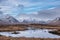 Beautiful Winter panorama landscape image of mountain range and peaks viewed from Loch Ba in Scottish Highlands with dramatic