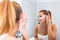 Beautiful woman applying anti-fatigue under-eye mask looking in mirror with smiley face using cream, touching face. self skin care