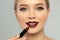 Beautiful woman applying dark lipstick on gray