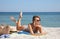 Beautiful woman with bag and other beach stuff on sand near sea