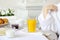 Beautiful woman behind a white table with fresh juice, a croissant, milk.