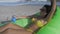 Beautiful Woman in Bikini Lights on Sea Beach Lies on Green Inflatable Pillow with Cocktail in Hand