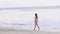 Beautiful woman in bikini walking on sandy shore on sea beach. Young woman enjoying summer walk on wet sand at beach