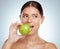 Beautiful woman biting into a green apple while posing with copypsace. Caucasian model looking contemplative while