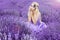 Beautiful woman with blond hair in a beautiful long white wedding dress stands on a field with heather flowers