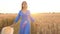 Beautiful woman in a blue dress and hat walking through a wheat field at sunset. Freedom concept. Wheat field in sunset