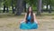 Beautiful woman in blue dress in lotus pose meditating in park, slow dolly pan