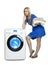 Beautiful woman in a blue dress next to a new washing machine holds a stack of clean laundry