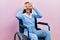 Beautiful woman with blue eyes sitting on wheelchair doing ok gesture like binoculars sticking tongue out, eyes looking through