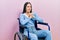 Beautiful woman with blue eyes sitting on wheelchair laughing nervous and excited with hands on chin looking to the side