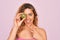 Beautiful woman with blue eyes wearing towel shower after bath holding kiwi fruit over eye very happy pointing with hand and