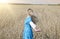 The beautiful woman in a blue long dress in the field of ripe ears of cereals