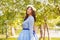 A beautiful woman in a blue puffy dress with a rim of white flowers on her head walks through the park between blooming apple tree