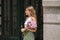 Beautiful woman with bouquet of flowers waits in the doorway of a house. Pretty young girl with a portrait on the street