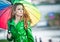 Beautiful woman in bright green coat posing in the rain holding a multicolored umbrella