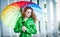 Beautiful woman in bright green coat posing in the rain holding a multicolored umbrella