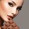 Beautiful woman with brown nails holds bar of chocolate