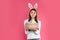 Beautiful woman in bunny ears headband holding basket with Easter eggs on color background