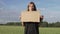 A beautiful woman with a cardboard poster stands in a field in the summer