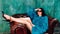 Beautiful woman in colorful green fur coat and big sunglases sitting in chair in high heel shoes. Fashion photo