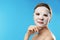 Beautiful woman with cotton mask sheet on face against color background