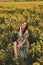 Beautiful woman with dark hair in elegant clothes posing in blooming rapeseed field