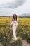 Beautiful woman with dark hair in elegant clothes posing in blooming rapeseed field
