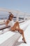 beautiful woman with dark hair in elegant white swimming suit and sunglasses posing on the terrace with cup of coffee