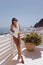 beautiful woman with dark hair in elegant white swimming suit and sunglasses posing on the terrace with cup of coffee