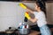 Beautiful woman with dark hair in protective yellow gloves cleaning kitchen with detergents.