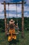 Beautiful woman with dark hair in yellow dress posing on the swing with Bali jungle view