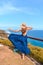 Beautiful woman with dark long hair in elegant blue dress posing in the cliff with ocean view