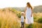 Beautiful woman in a dress walks in nature with her son with curly hair.