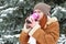 Beautiful woman drinking a hot drink and keep warm on winter outdoor, snowy fir trees in forest, long red hair, wearing a sheepski