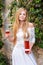 Beautiful woman drinking wine outdoors. Portrait of young blonde beauty in the vineyards having fun, enjoying a glass of