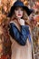 Beautiful woman in elegant black hat with large fields and bright red lipstick on her lips in a coat walks in the park near
